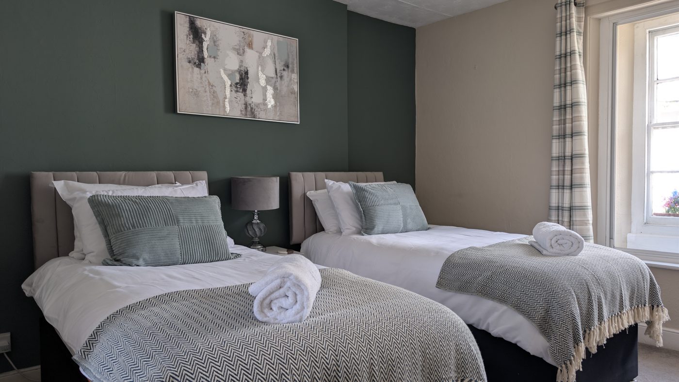 Room 1, the twin — two single beds, dark green feature wall and a bright sash window