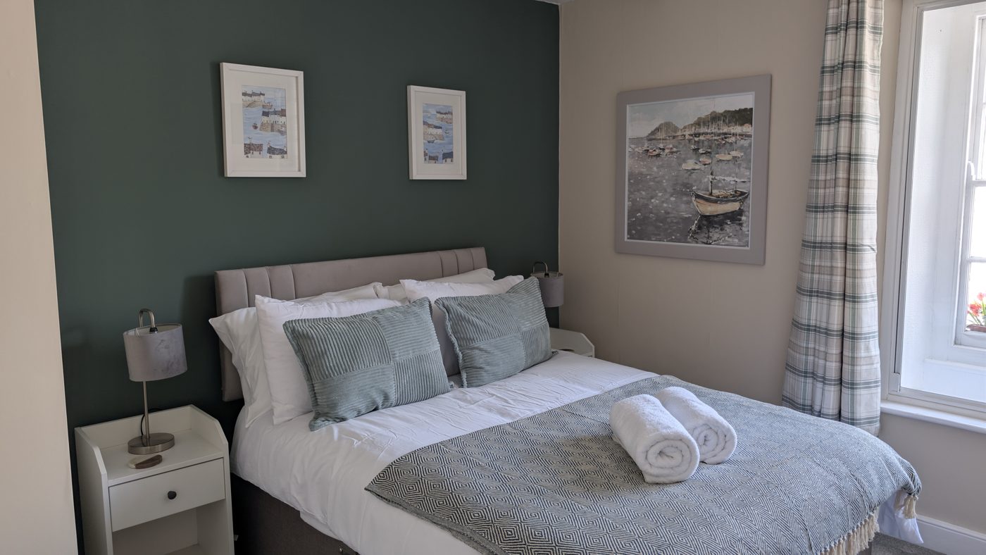 Room 2, Carbis — a freshly refurbished double room at The Bugle Inn with a dark green feature wall, crisp white linen and Cornish harbour artwork