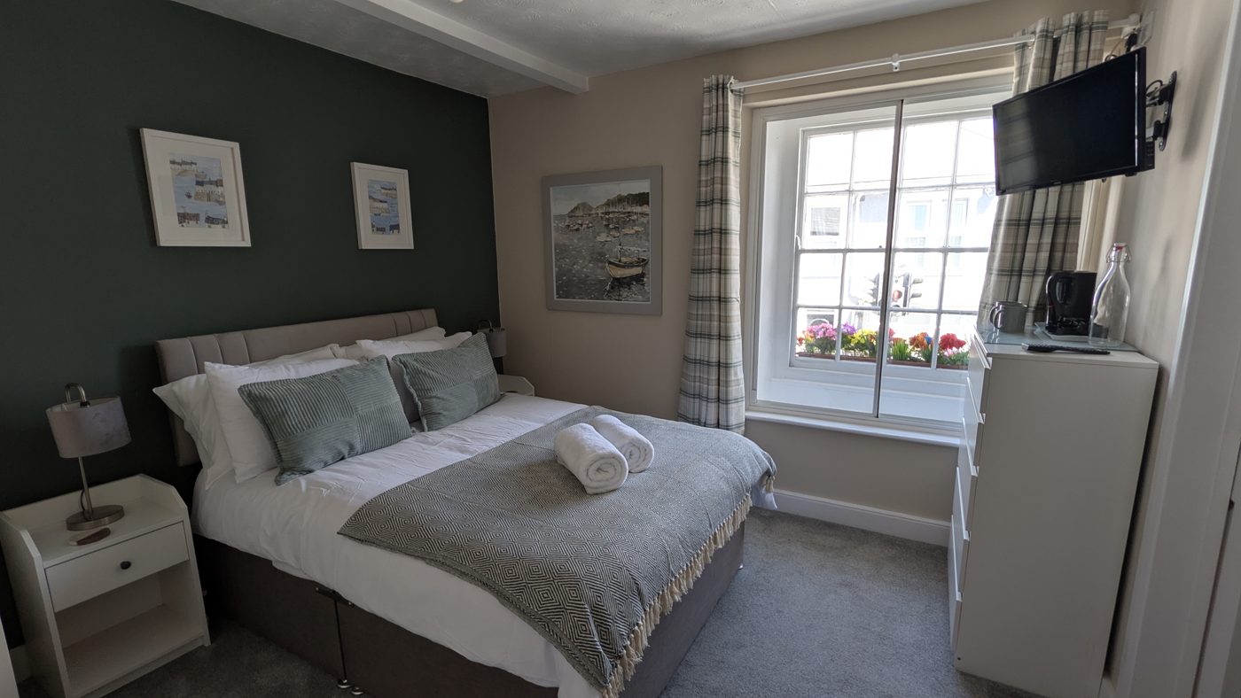 Room 2, the beamed double — dark green wall, white linen and Cornish harbour painting